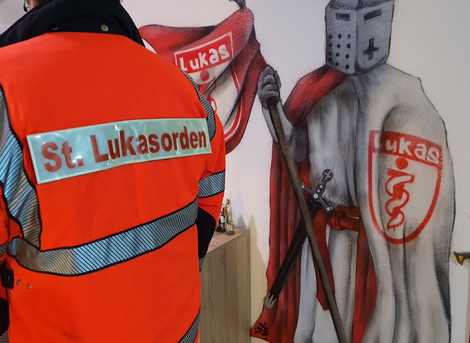 Einsatzkraft des St. Lukasordens vor einem Wandbild des Ordens